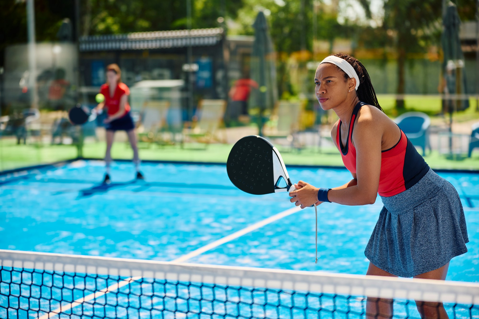 Black female athlete playing padel tennis doubles match on outdoor court.